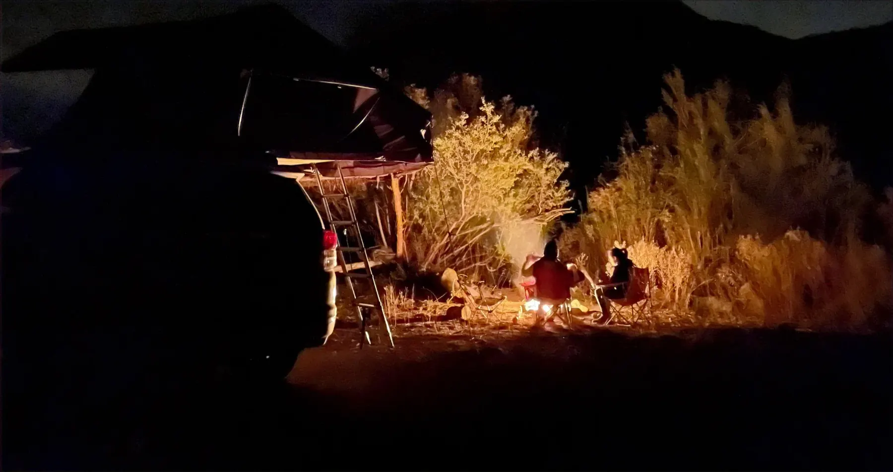 Fogata nocturna junto a una camioneta con carpa de techo